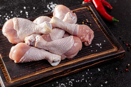 Raw meat. Chicken legs lie on a wooden board with vegetables and spices on a black background. background image, copy space textの写真素材