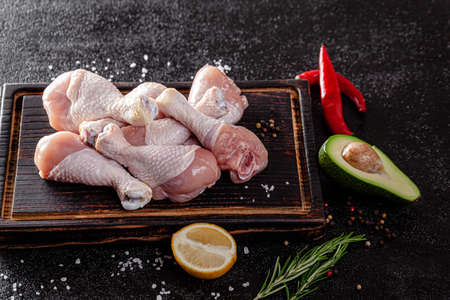 Raw meat. Chicken legs lie on a wooden board with vegetables and spices on a black background. background image, copy space textの写真素材