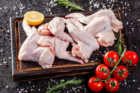 Raw meat. Chicken wings lie on a wooden board with vegetables and spices on a black background. background image, copy space textの写真素材