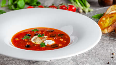 Ukrainian cuisine in European style. Solyanka soup with assorted sausages and meat. Beautiful serving dish in a restaurant in a white plate. background image, copy space textの写真素材