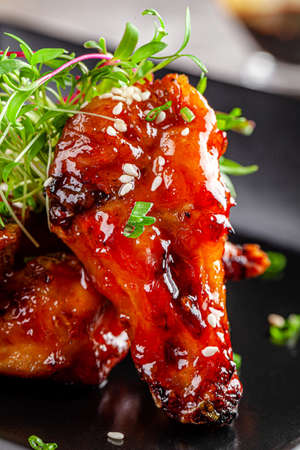 American cuisine. Juicy fried chicken wings glazed with sesame seeds and herbs. Beautiful serving dish in a restaurant in a black plate. background image, copy space textの写真素材