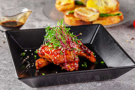 American cuisine. Juicy fried chicken wings glazed with sesame seeds and herbs. Beautiful serving dish in a restaurant in a black plate. background image, copy space textの写真素材