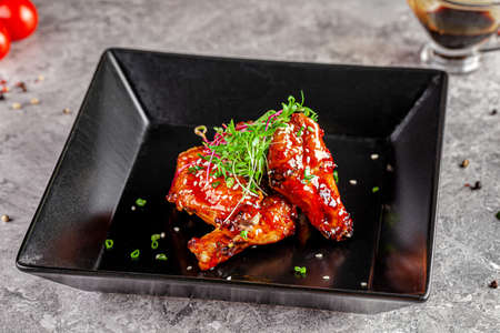 American cuisine. Juicy fried chicken wings glazed with sesame seeds and herbs. Beautiful serving dish in a restaurant in a black plate. background image, copy space textの写真素材