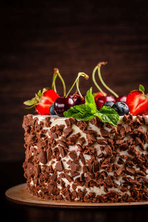 Chocolate sponge cake with white cream and berries, strawberries, cherries and mint. Cake cutaway on cinnamon background. copy spaceの写真素材