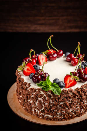 Chocolate sponge cake with white cream and berries, strawberries, cherries and mint. Cake cutaway on cinnamon background. copy spaceの写真素材