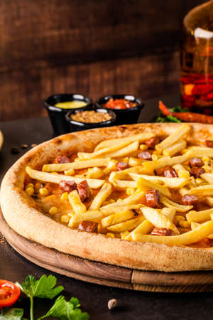 Italian Cuisine. Thin Oktoberfest pizza with french fries, hunting sausages and corn. Background image. copy spaceの写真素材