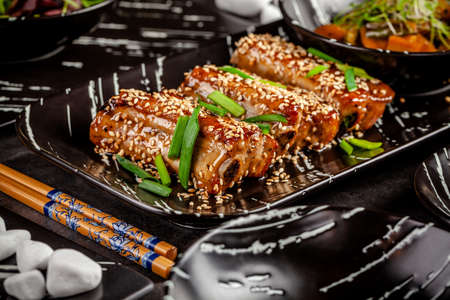 Asian food. Fried pork ribs in sweet and sour sauce with sesame seeds. Beautiful dish in a restaurant in a flat black plate. Background image. copy spaceの写真素材