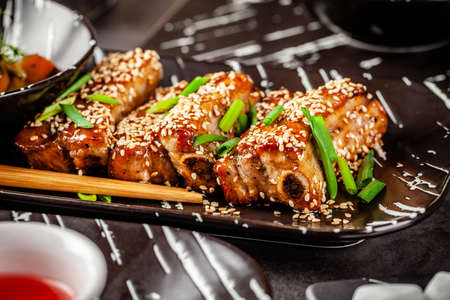 Asian food. Fried pork ribs in sweet and sour sauce with sesame seeds. Beautiful dish in a restaurant in a flat black plate. Background image. copy spaceの写真素材