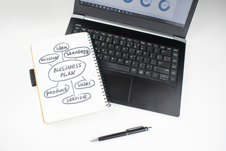 Minimalistic workplace concept, with a laptop, pen and business work records on a white background. Image of business plan, startup. Top view. Flat lay styleの写真素材