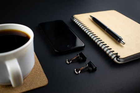 Minimalistic workplace concept, with a smartphone, pen and business work records on a dark background. Image of business plan, startup. Close up imageの写真素材