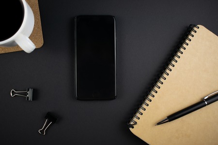 Minimalistic workplace concept, with a smartphone, pen and business work records on a dark background. Image of business plan, startup. Top view. Flat lay styleの写真素材