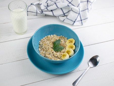 Plate with tasty oatmeal and banana slices on white wood background. Concept image of breakfast, healthy eatingの写真素材