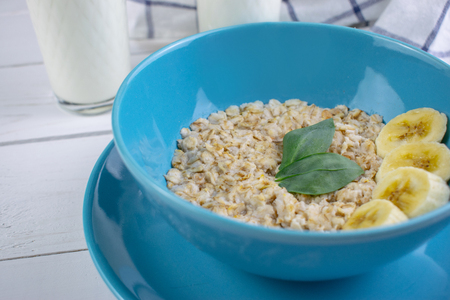 Plate with tasty oatmeal and banana slices on white wood background. Concept image of breakfast, healthy eatingの写真素材