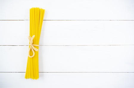 Bunch of long dry spaghetti on a white wooden table. Italian cuisine concept, food ingredients. Flat lay. Top view, copy space.の写真素材