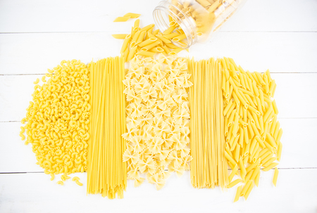 Various types of pasta on a white wooden table. Italian cuisine concept, food ingredients. Flat lay. Top view, copy space.の写真素材