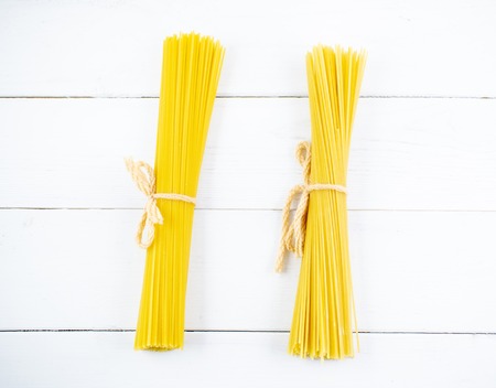Bunch of long dry spaghetti on a white wooden table. Italian cuisine concept, food ingredients. Flat lay. Top view, copy space.の写真素材