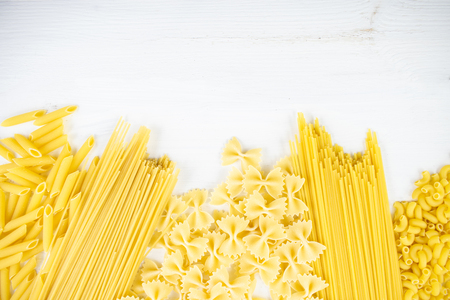 Various types of pasta on a white wooden table. Italian cuisine concept, food ingredients. Flat lay. Top view, copy space.の写真素材