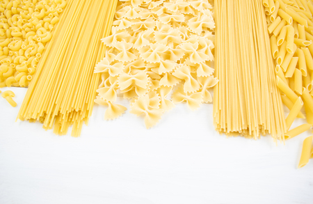 Various types of pasta on a white wooden table. Italian cuisine concept, food ingredients. Flat lay. Top view, copy space.の写真素材