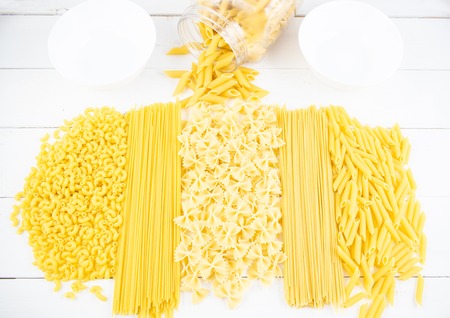 Various types of pasta on a white wooden table. Italian cuisine concept, food ingredients. Flat lay. Top view, copy space.の写真素材