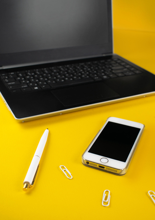 Minimalistic workplace concept, with a smartphone, pen and business work records on a yellow background. Image digital agency, online education. Close up image.の写真素材