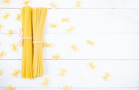 Bunch of long dry spaghetti on a white wooden table. Italian cuisine concept, food ingredients. Flat lay. Top view.の写真素材