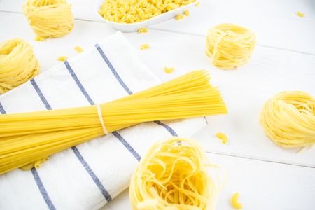 Various types of pasta on a white wooden table. Italian cuisine concept, food ingredients. Flat lay. Top view.の写真素材