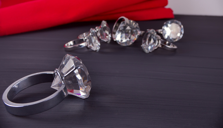 Big diamond ring on the table. In the background a bunch of rings and red table napkinの写真素材