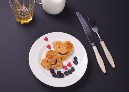 plate of two pancakes in the shape of heart with berries on black tableの写真素材
