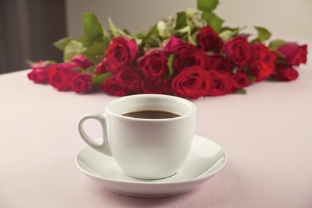 A cup of coffee and roses on the tableの写真素材