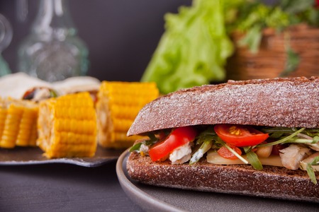 Baguette sandwich with turkey breast, cheese, lettuce, arugula, tomatoes and onion on a black plate on the tableの写真素材