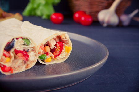 Burrito rolls with vegetables on a gray plate on black table and vegetables, cherry tomatoes and garlic at backgroundの写真素材