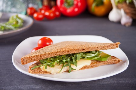 Sandwich with turkey breast, cheese, lettuce, arugula, tomatoes and onion on a black plate on the tableの写真素材