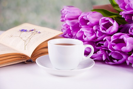 A cup of tea, book and violet tulips on the white tableの写真素材