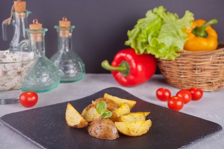 Homemade baked organic potato wedges with herbs on a plate with fresh vegetables on the backgroundの写真素材