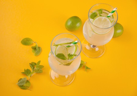 Lemonade or mojito cocktail with lemon and mint, cold refreshing drink or beverage with ice on yellow background. Top view.の写真素材