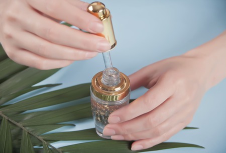 Woman's hand holding pipette with liquid in which gold particles are visible. Palm leaf in a background.の写真素材