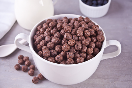 A bowl of dry chocolate balls cereal and bottle if milk on the gray table for health breakfast for adult and kidsの写真素材
