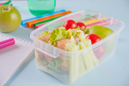 Food in the office or at school. Lunch box with healthy food on the desktop with notebook, felt pens, apple and bottles on the backgroundの写真素材