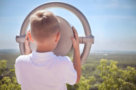 little boy in white t-shirt using tourist viewer operated binoculars outside, rear view