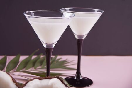 Two glasses of Pina Colada tropical cocktail on the pink table with palm leaf and coconutの写真素材