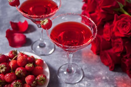 Two red fresh exotic alcoholic cocktail in clear glasses, red roses and plate with strawberry for romantic dinnerの写真素材