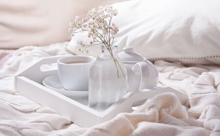 Close up of cup of tea, milk, teapot and bouquet of white flowers on the white tray in the bed. Summer romantic morning.の写真素材