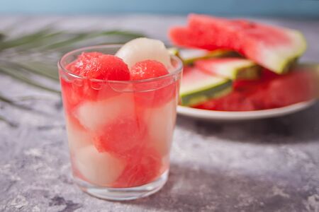 Fruit salad with melon and watermelon balls in glass and pice of watermelon under the palm leaf on the concreate backgroundの写真素材