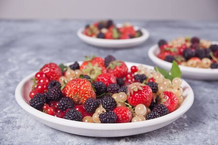 Healthy mixed berry with strawberry, blackberry, red and white currant on the different white plates on concrete background. Top view. Copy space.の写真素材