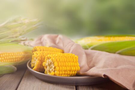 Boiled sweet corn on a plate on the wooden table. Top view.