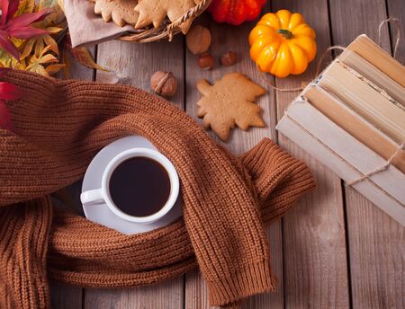 Cozy and warm composition with cup of coffee, autumn leaves, books, pumpkin, homemade cookies and sweater on the wooden table. Autumn concept. Top view.の写真素材