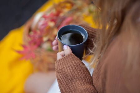Outdoors autumn picnic. Young woman holding mug of hot coffee in a hand.の写真素材