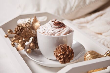 Cup of cocoa on the white tray on the bed early winter morning. Golden decoration on the background.