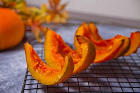 Fresh pumpkin cut in pieces of a oven metal baking rack with herbs and spices with colorful autumn leaves on the background.の写真素材