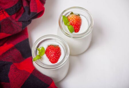 Two portions natural homemade yogurt in a glass jar with fresh strawberry with red checkered napkin on the white background. Top view.の写真素材